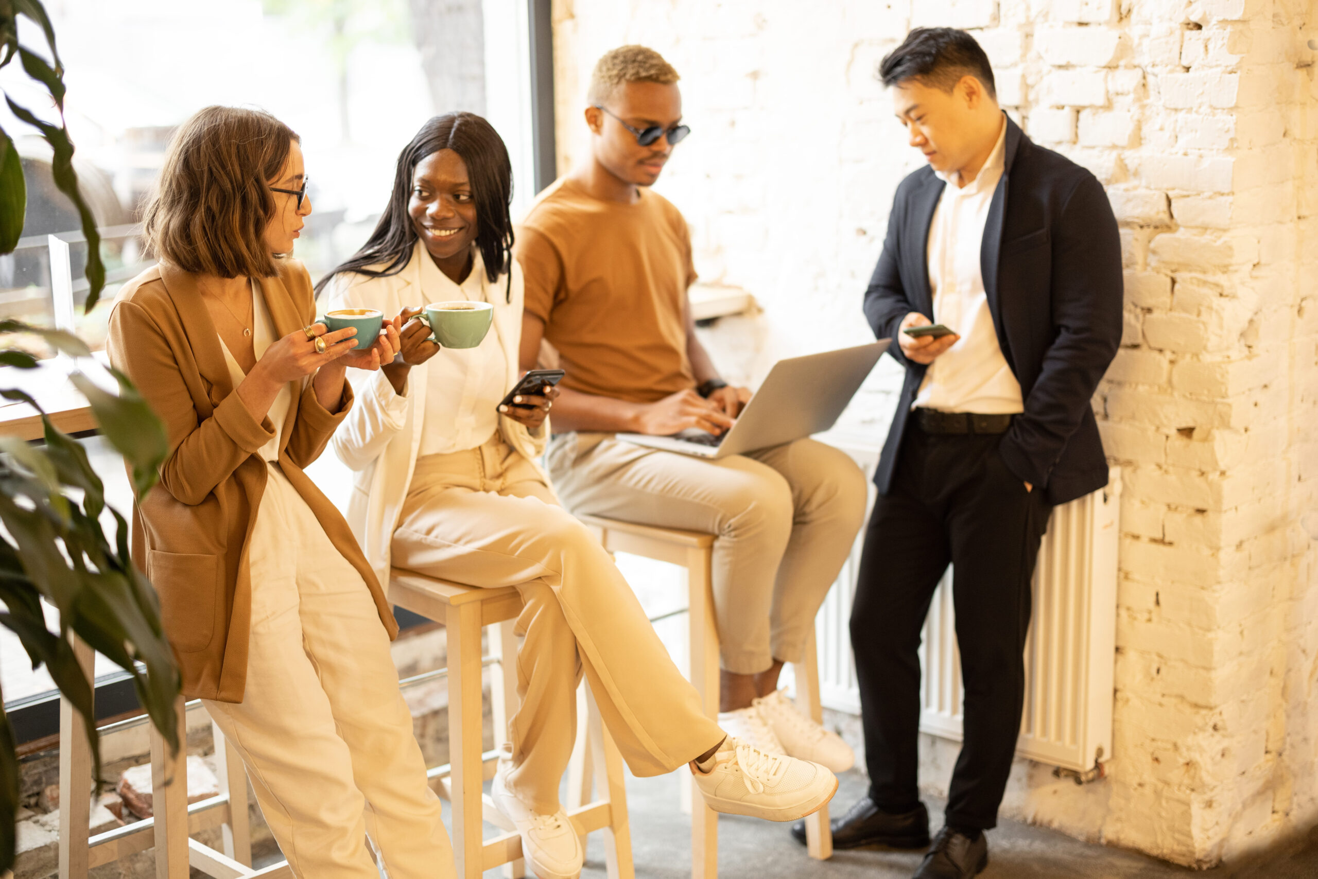 Multiracial business team having break during work in cafe or restaurant. Concept of rest on work. Women drinking tea and talking. Men using digital gadgets. Idea of business cooperation